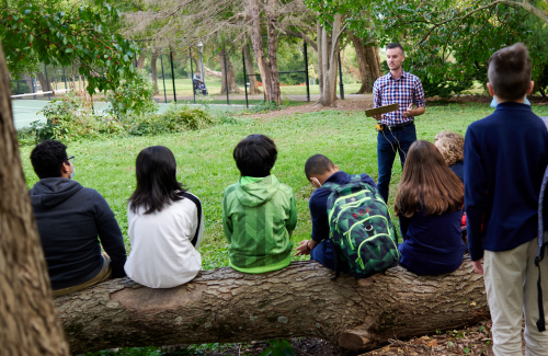 youth sitting on a log surrounded by trees listening to educator instructions